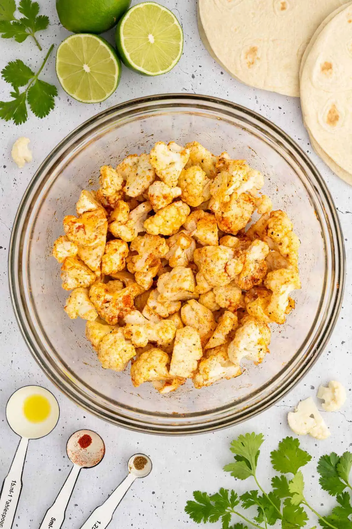 Seasoned cauliflower florets evenly coated with spices in a glass mixing bowl.