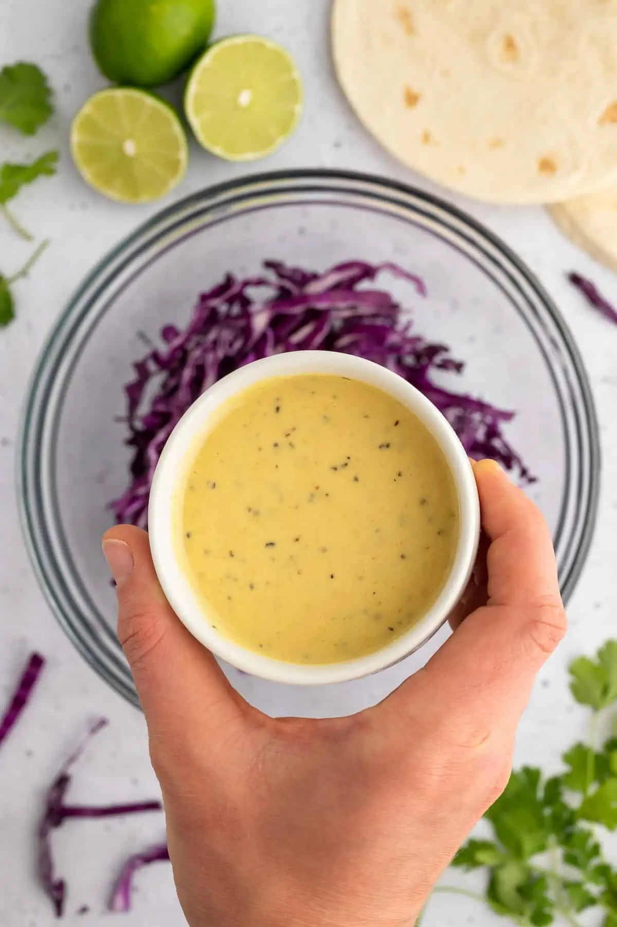 Small bowl of creamy vegan dressing held above shredded purple cabbage for slaw.
