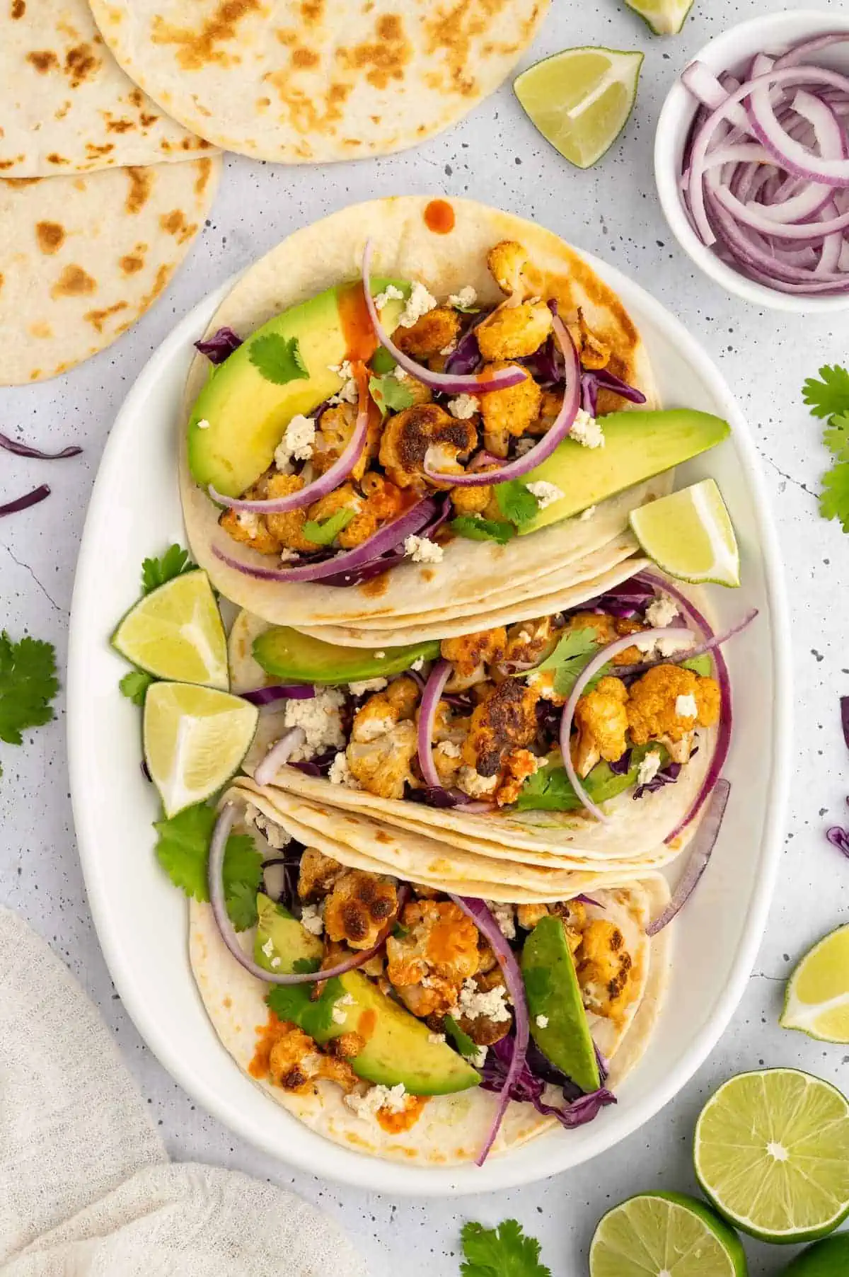A taco platter featuring vegan cauliflower tacos with lime wedges and fresh toppings.