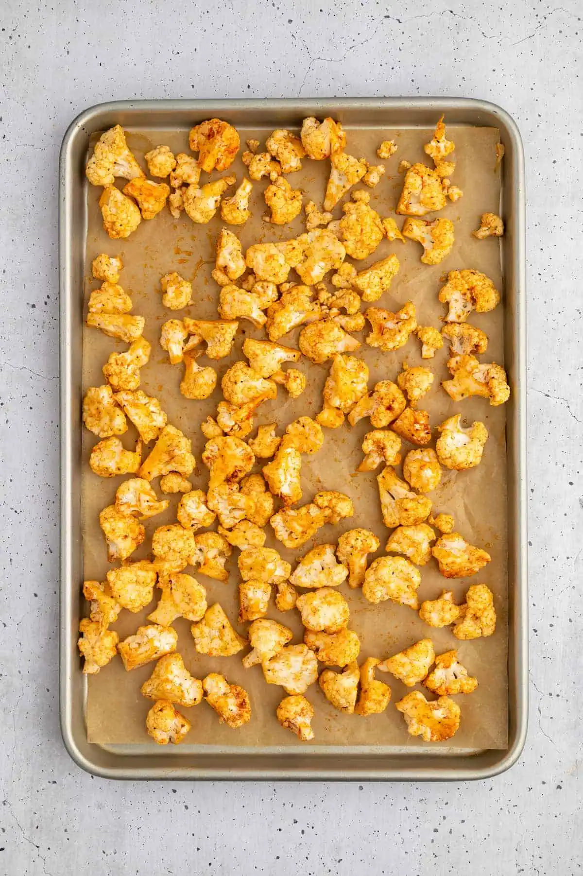 Seasoned cauliflower florets spread on a parchment-lined baking sheet before roasting.