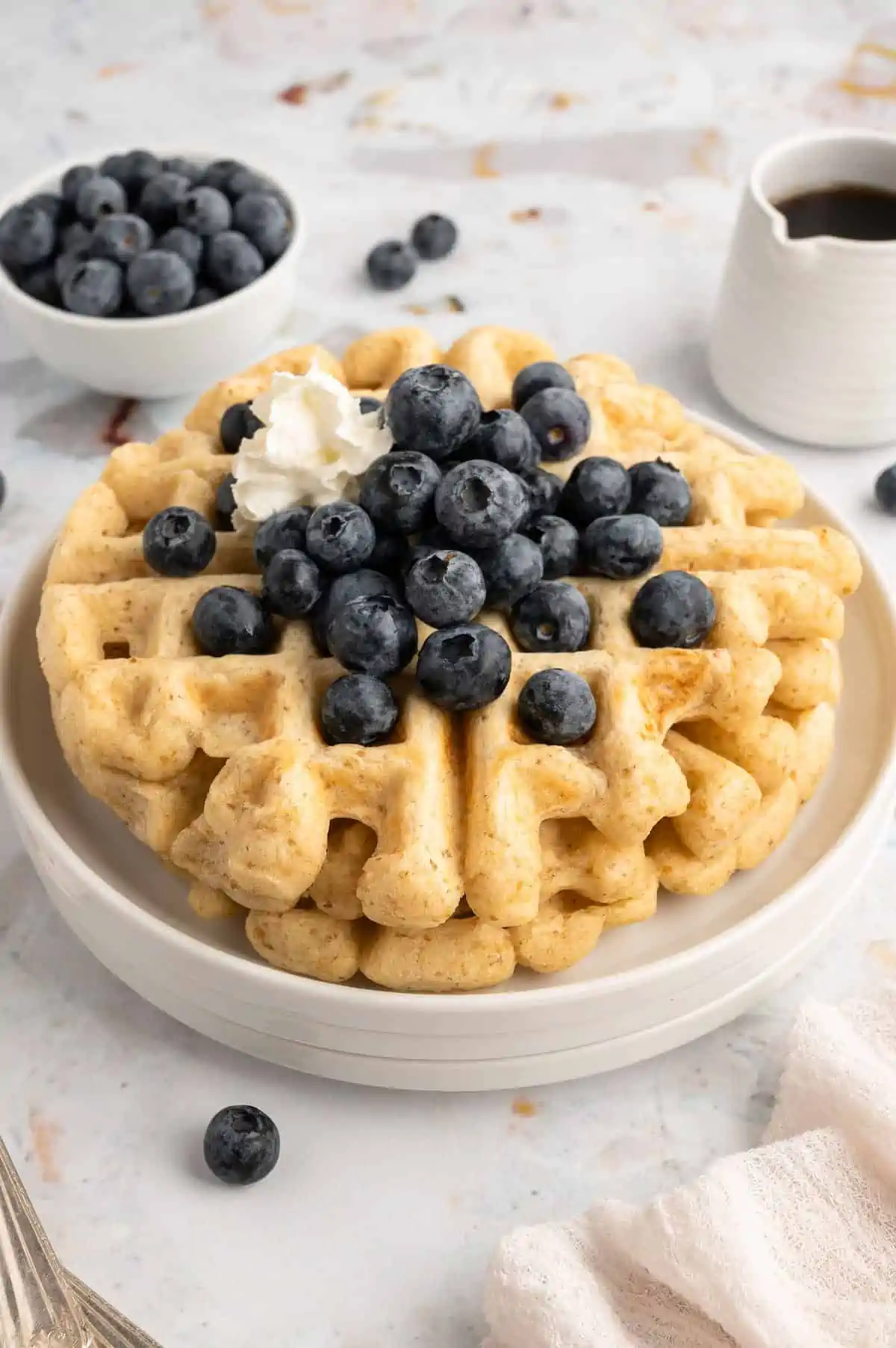 A stack of fluffy vegan belgian waffles with syrup, fruit, and plant-based butter on top.
