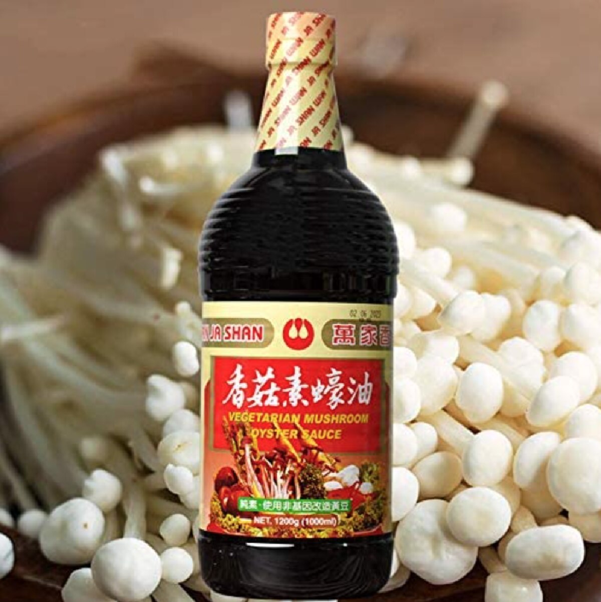 A dark, red and yellow bottle of Wah Ja Shan vegetarian oyster sauce against a background of tiny Enoki mushrooms in a wooden bowl.