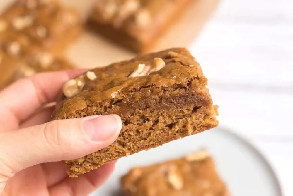 A hand holding a square of vegan blondie with maple and walnuts.
