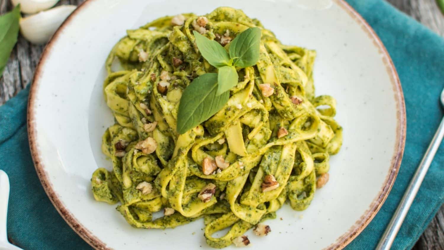 Close-up of vegan walnut pesto pasta garnished with fresh basil leaves.