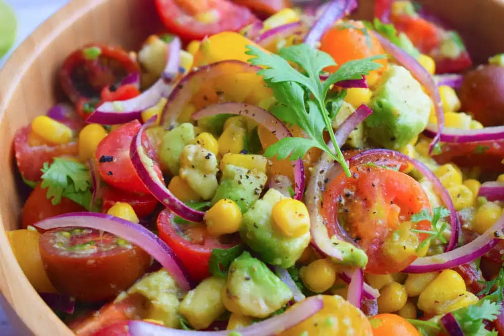 Corn and tomato salad with red onions in a bowl.