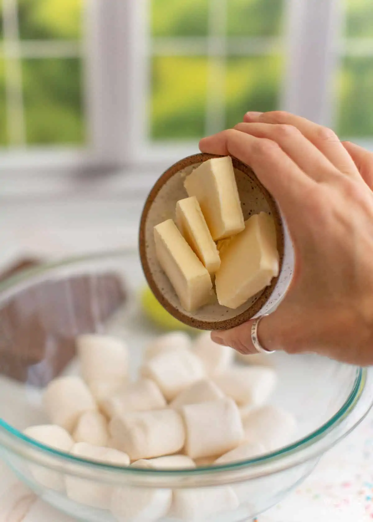 Adding butter to a large bowl of marshmallows.