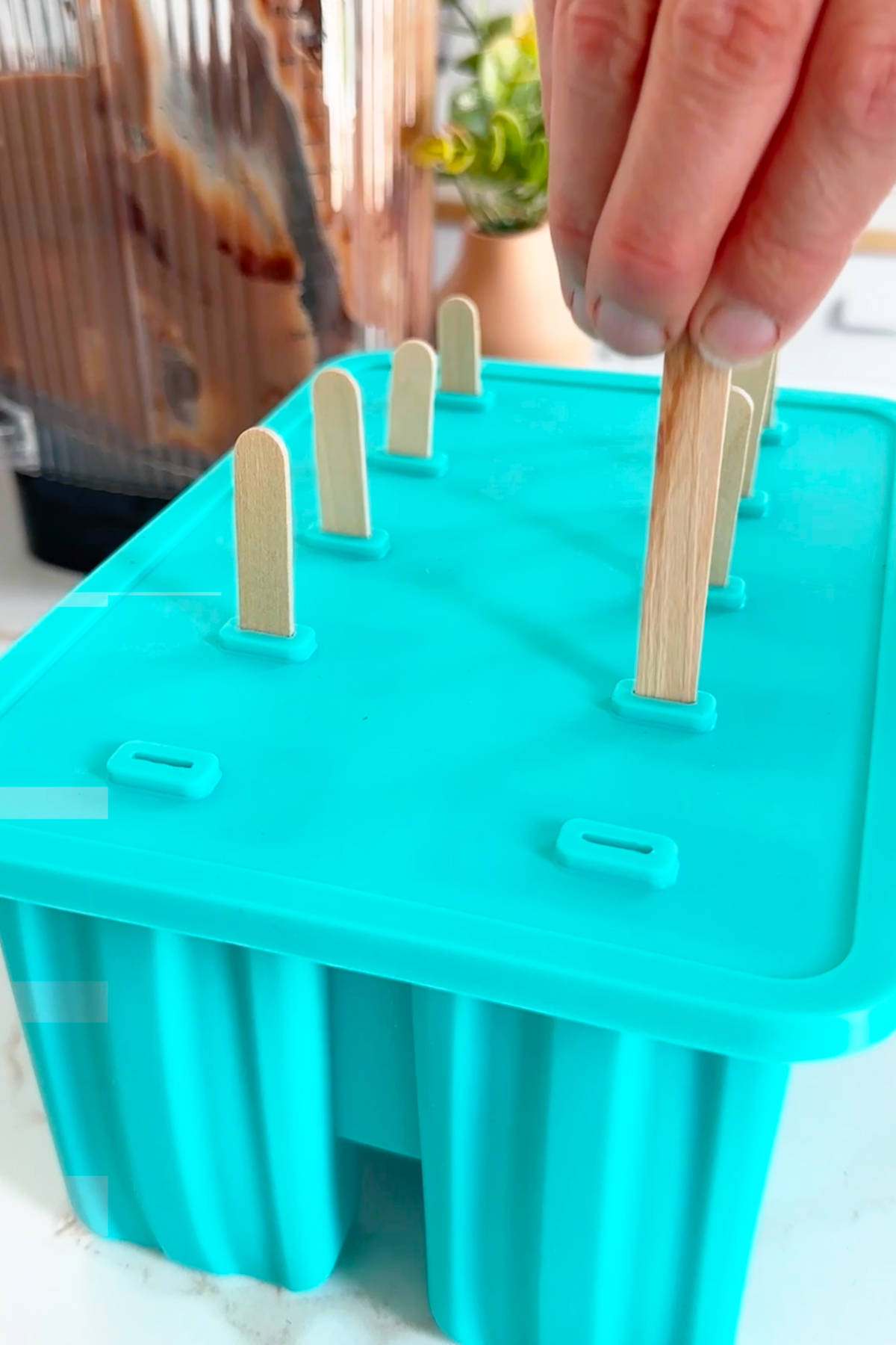 Placing the popsicles into the mold filled with the fudgesicle mixture.