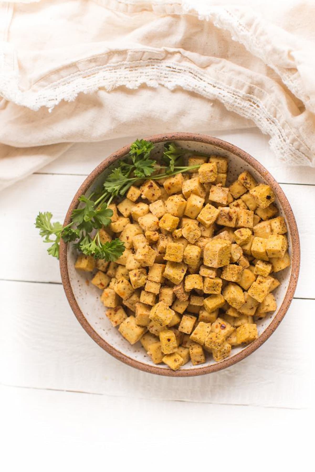 A bowl of air fryer tofu nuggets with a parsley sprig.