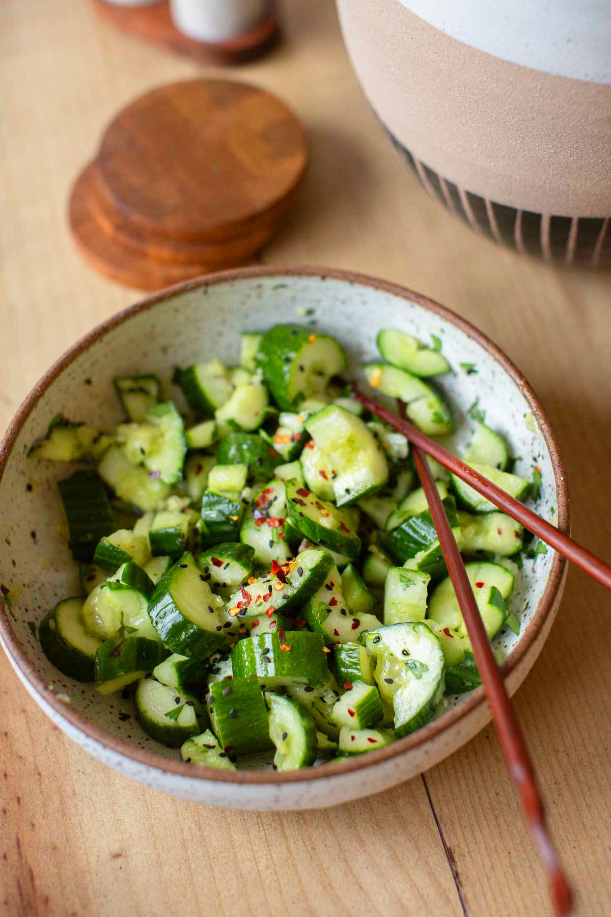 A bowl of spicy asian cucumber salad served with chopsticks.