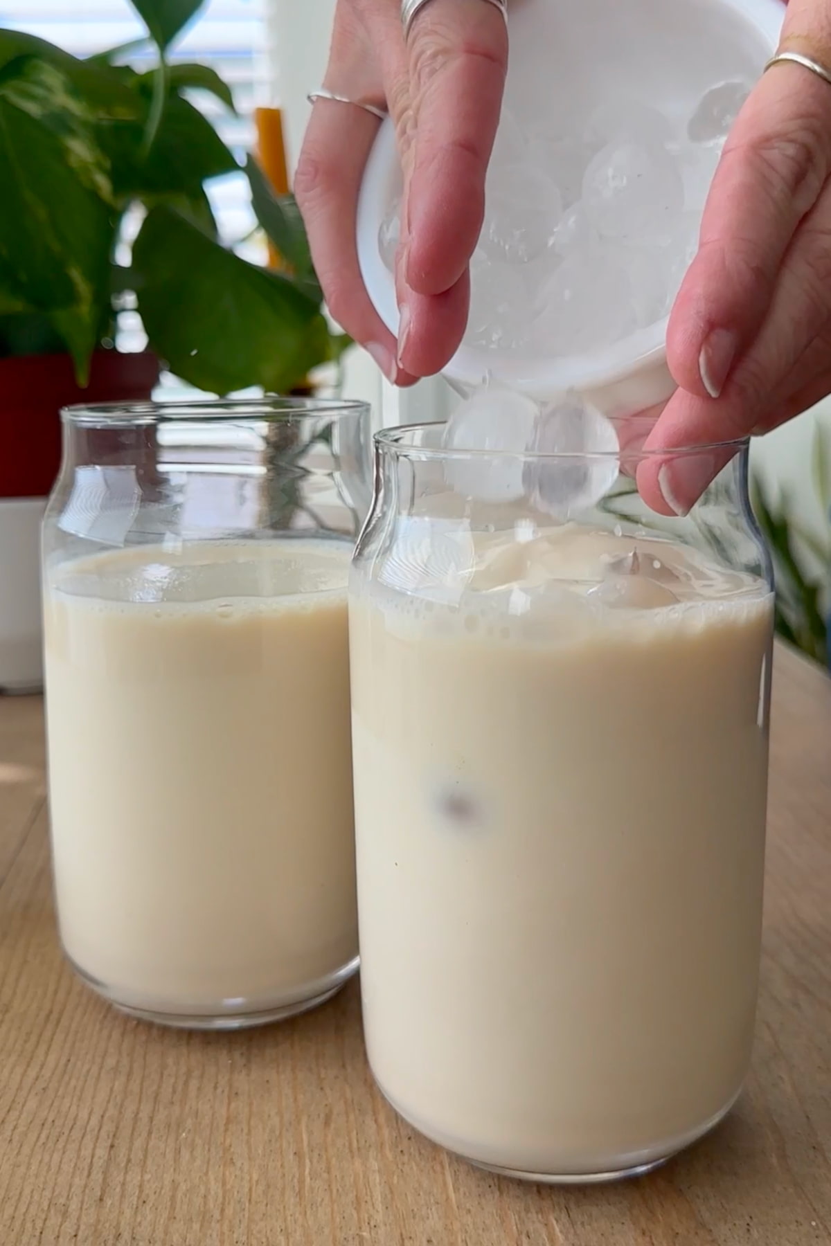 Hands holding a bowl of ice cubes that are pouring into a glass of plant-based milk.