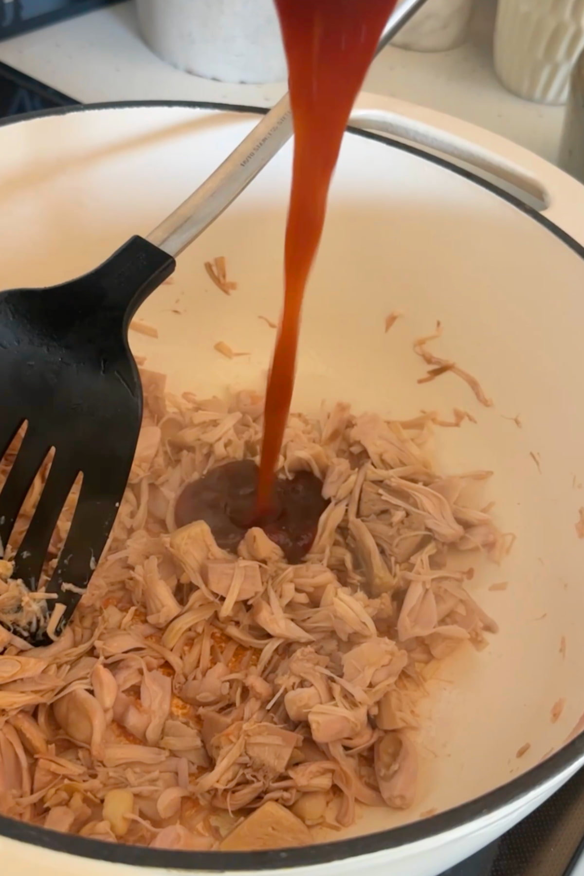 BBQ sauce pouring over shredded jackfruit in a pan.