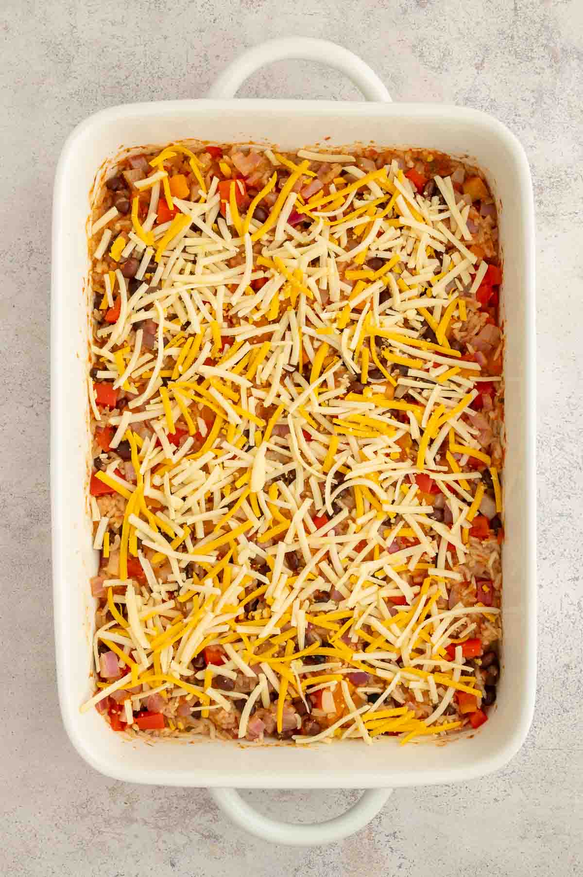 Baked bean and rice casserole with shredded cheese on top before the cheese has baked.