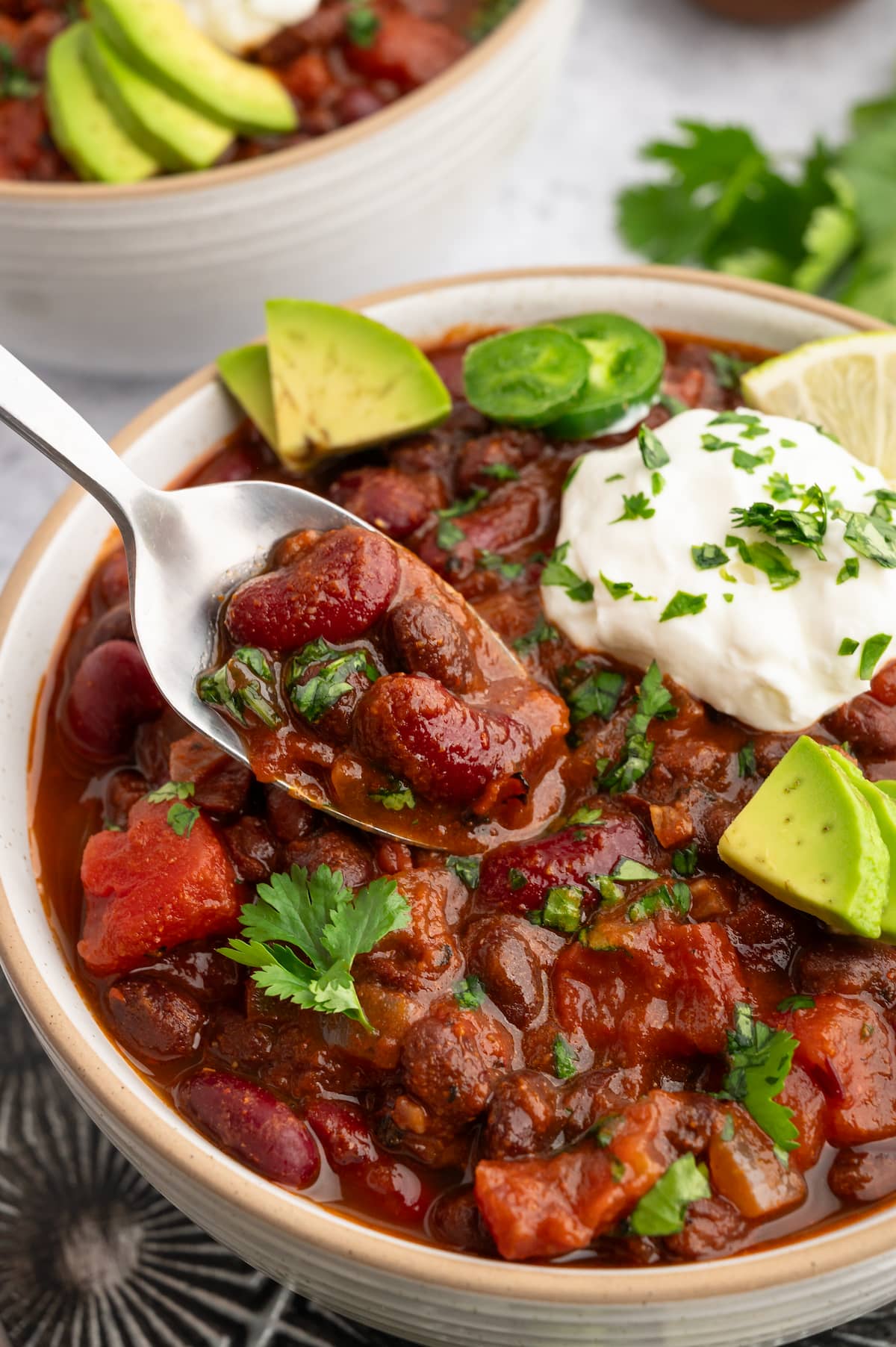 A spoon full of vegan chili hovering over a bowl of chili.