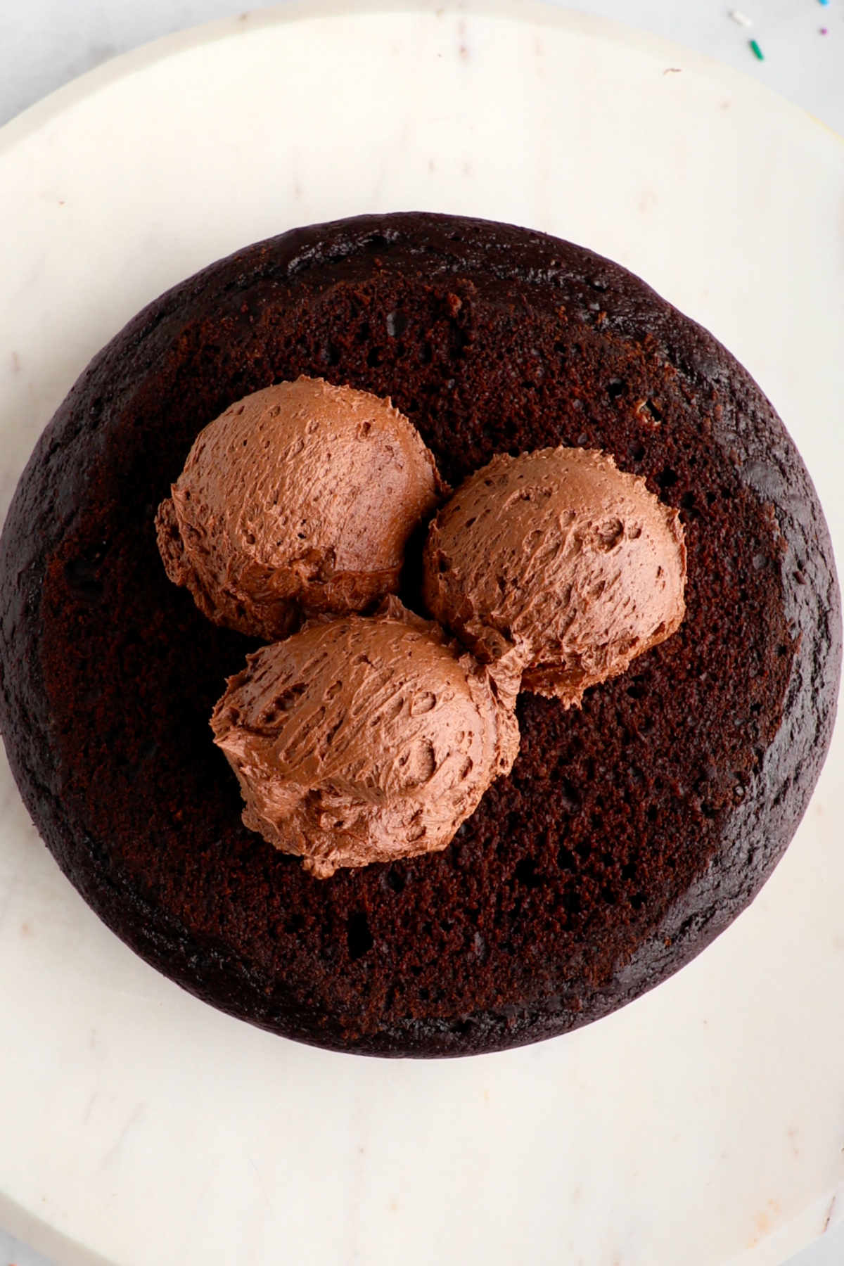 Three scoops of vegan chocolate frosting on top of a vegan cake.