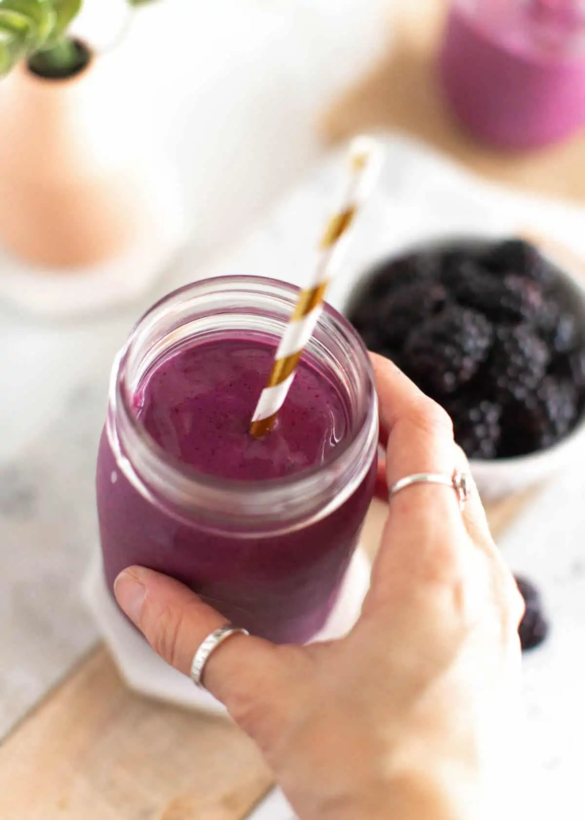 Hand holding a blackberry smoothie in a mason jar.