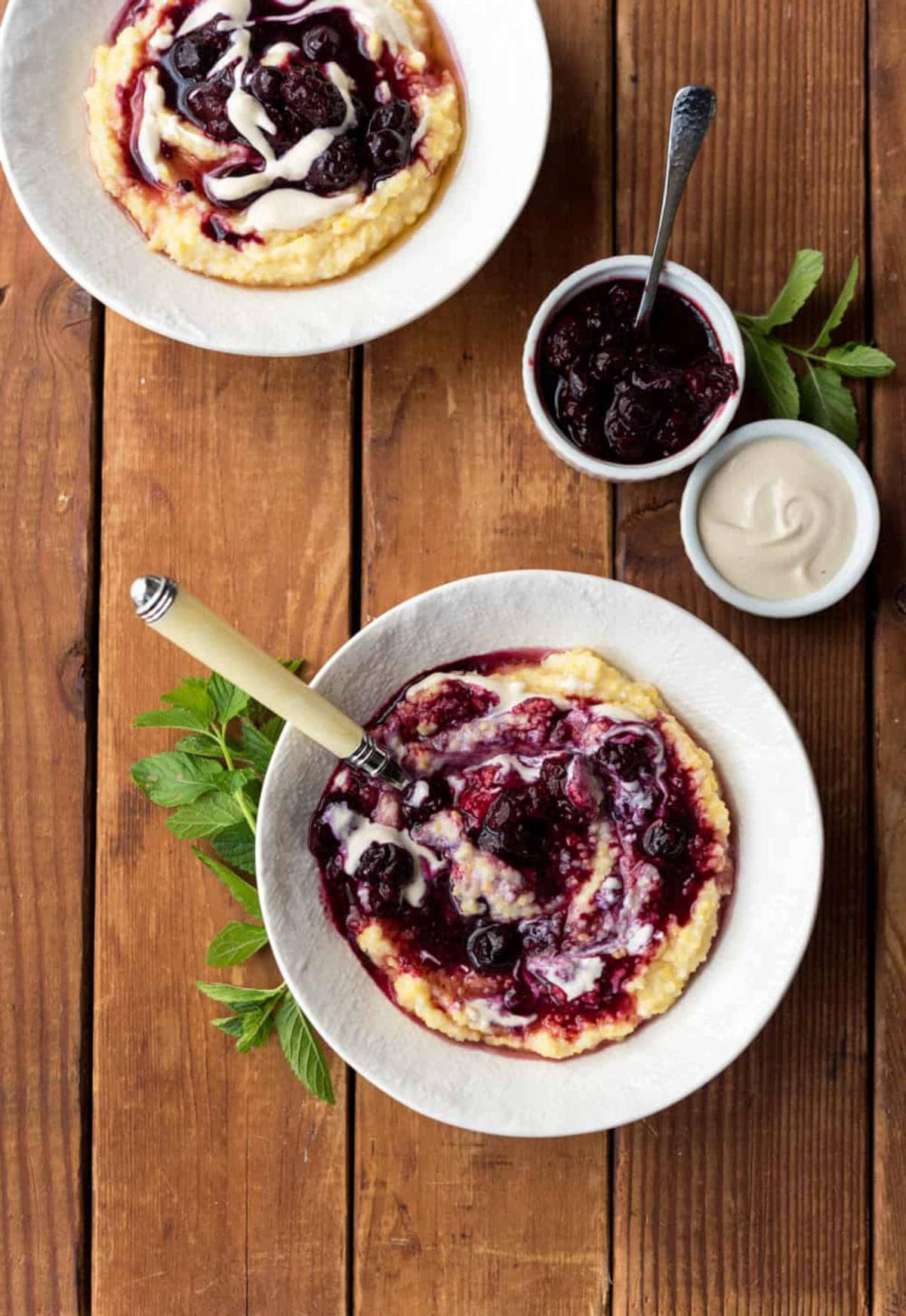 Two bowls of breakfast polenta topped with berries and cashew cream.
