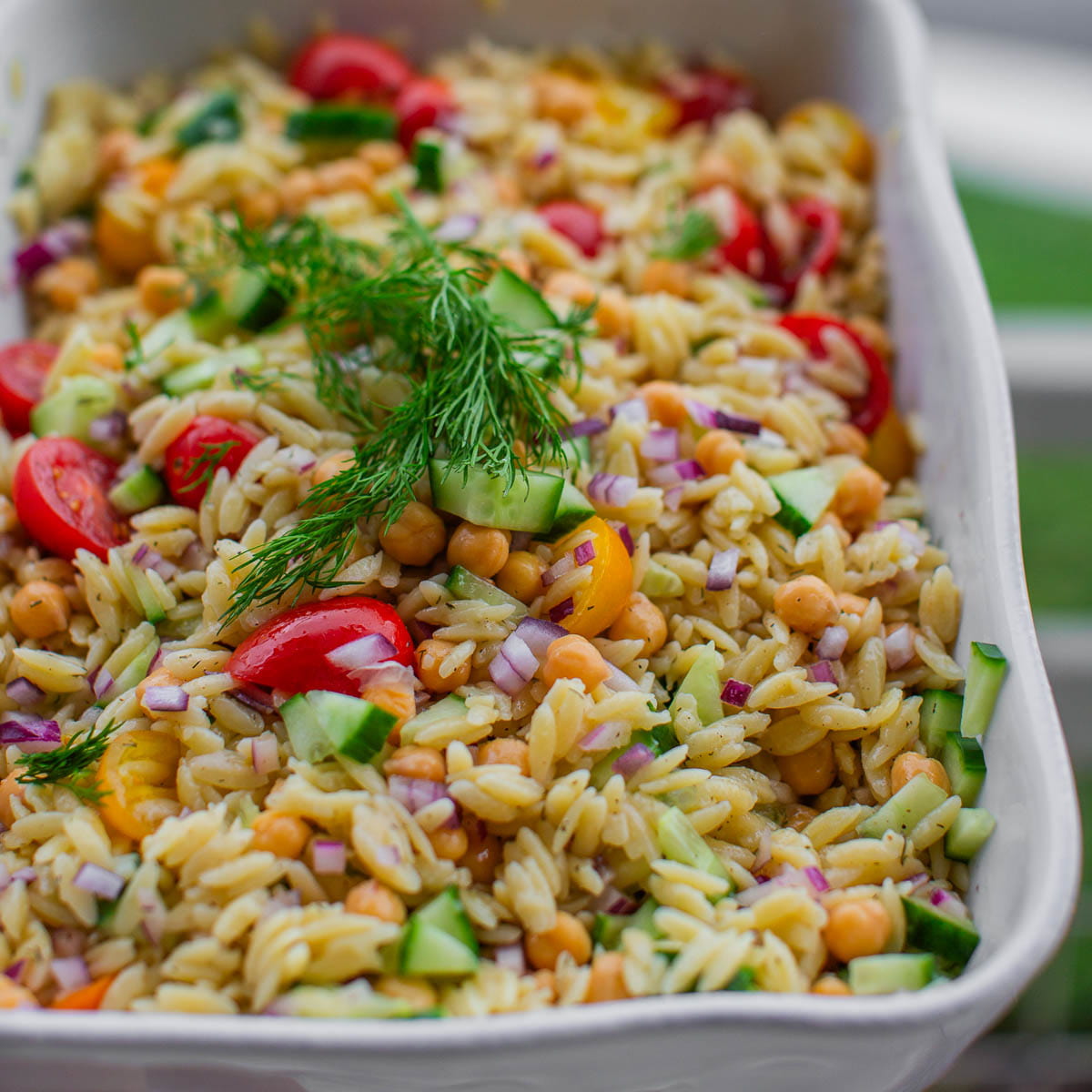 A serving dish filled with chickpea orzo salad and topped with fresh dill.