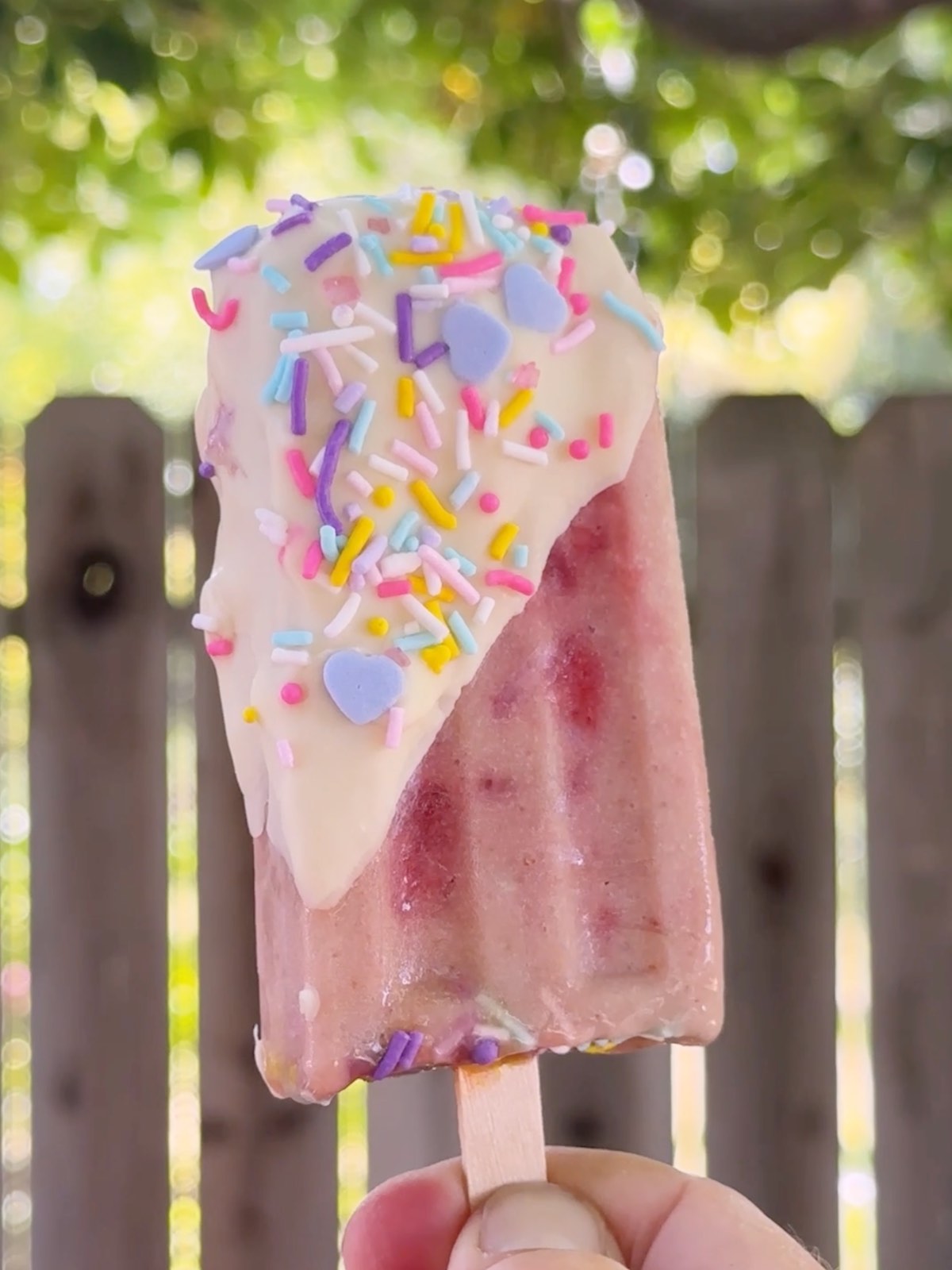 Strawberry banana popsicle dipped in vegan white chocolate and coated in colorful rainbow sprinkles.
