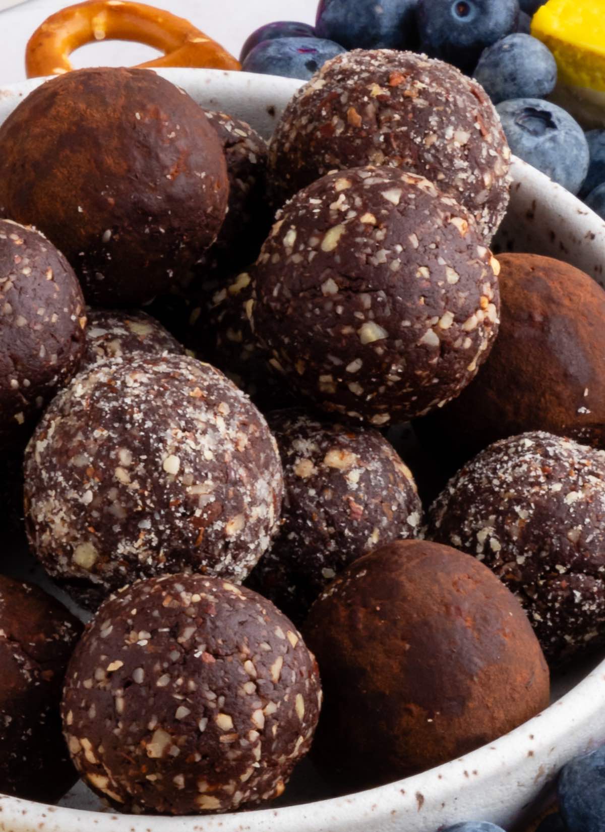 A bowl of vegan protein balls with some coated in cocoa powder and some coated in chopped nuts.