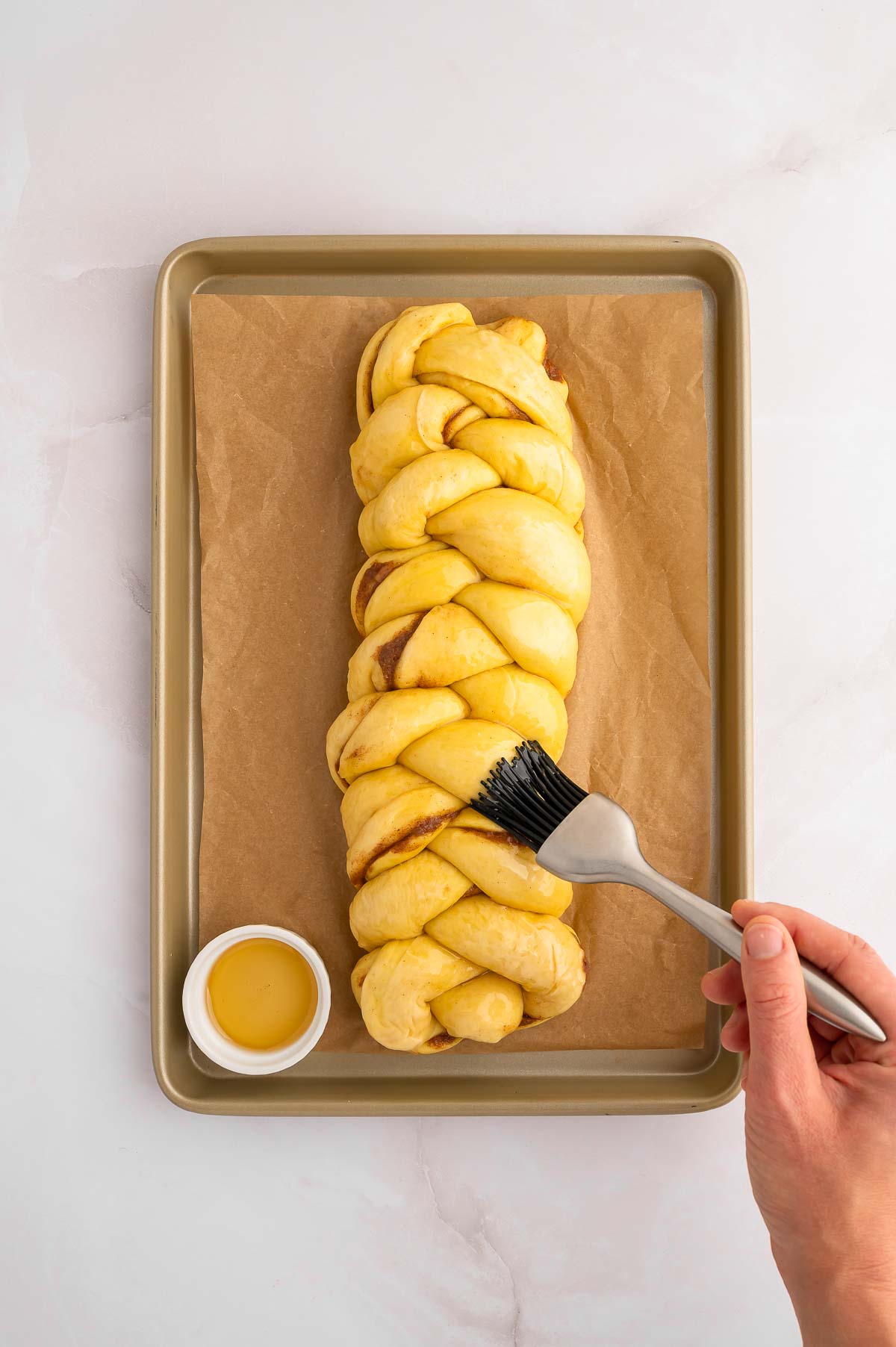 A braided loaf of vegan cinnamon challah being brushed with agave.