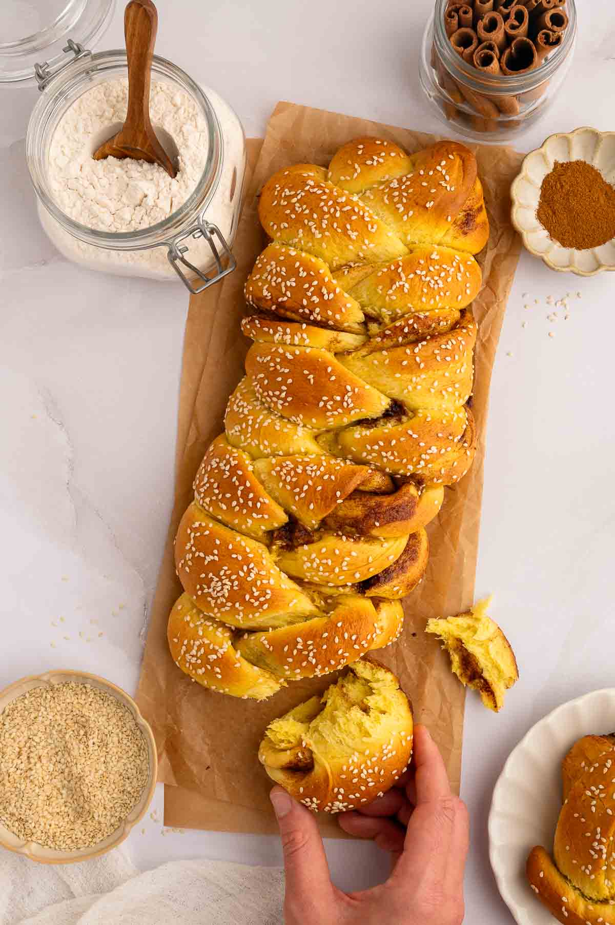 A hand pulling a piece off of a loaf of cinnamon challah.