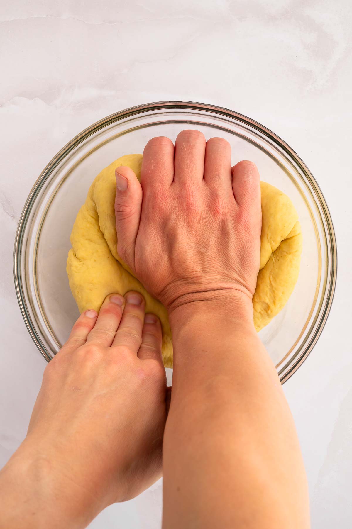 A hand kneading dough in a bowl.