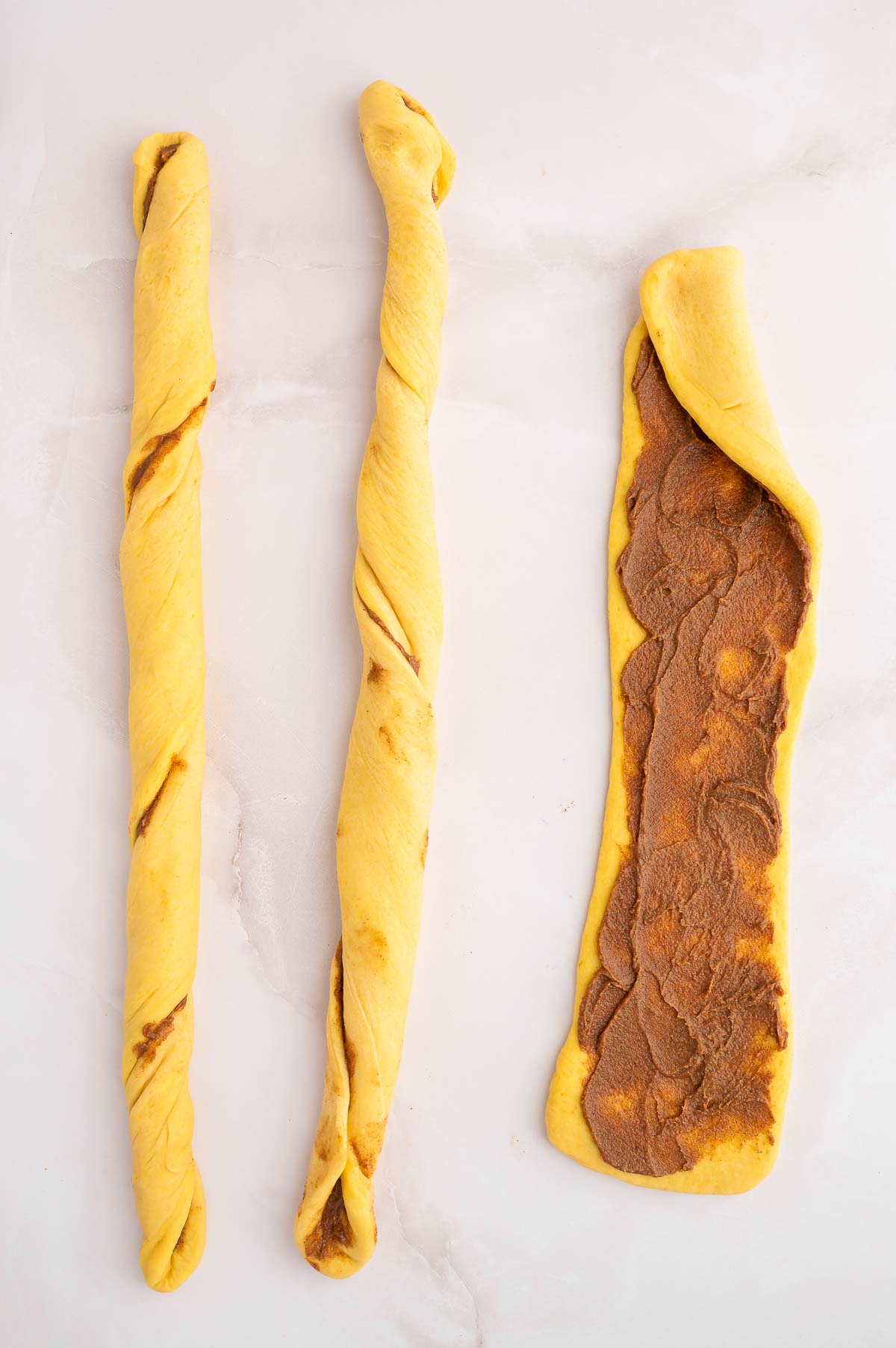 Cinnamon challah dough divided into 3 portions with filling spread.