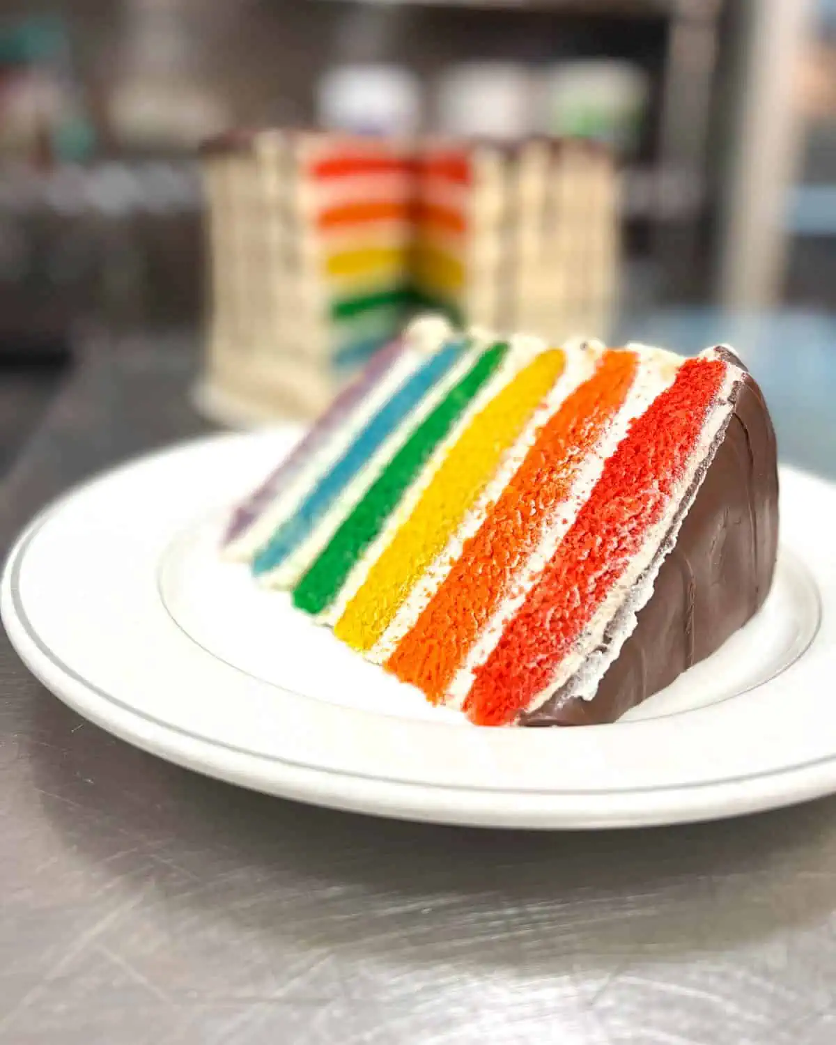 A slice of vegan wedding cake with rainbow colors and chocolate frosting.