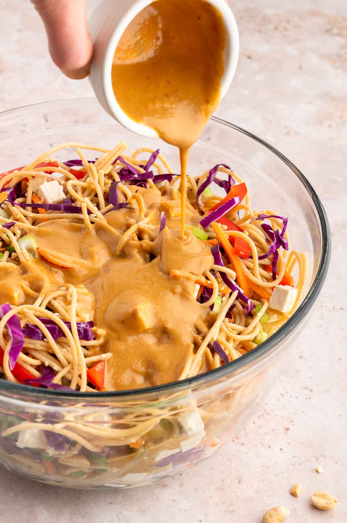 A hand pouring the peanut sauce over the cold noodle salad.