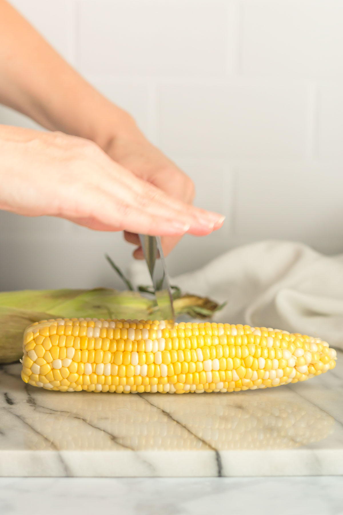 A corn cob being cut with a knife.