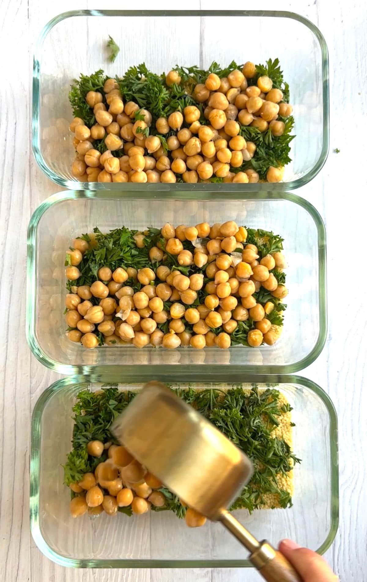 Fresh parsley and chickpeas layered on top of the couscous and vegetable bouillon in meal prep containers.