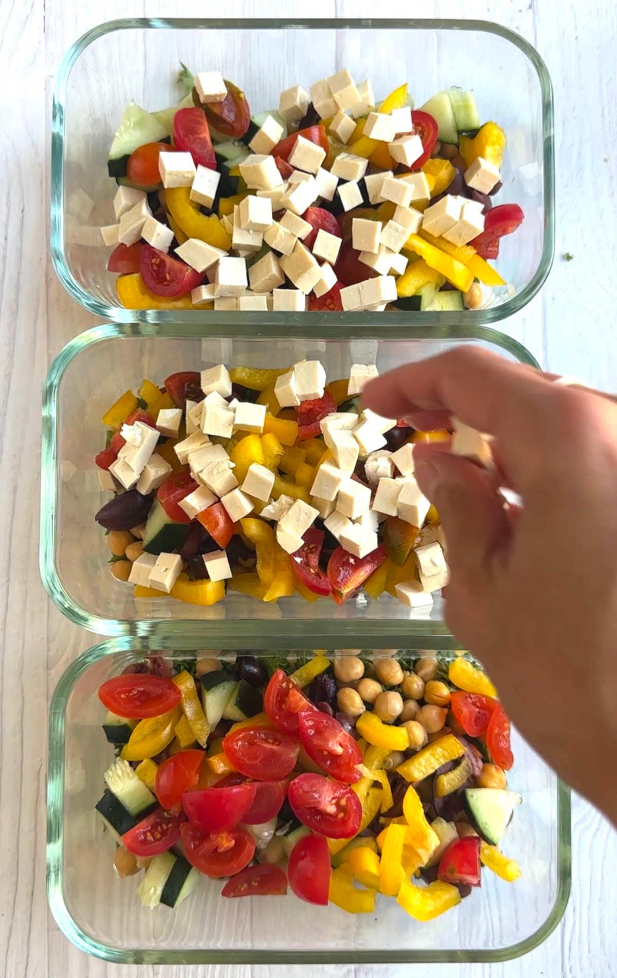 Tofu layered on top of all the vegetables and couscous in meal prep containers.