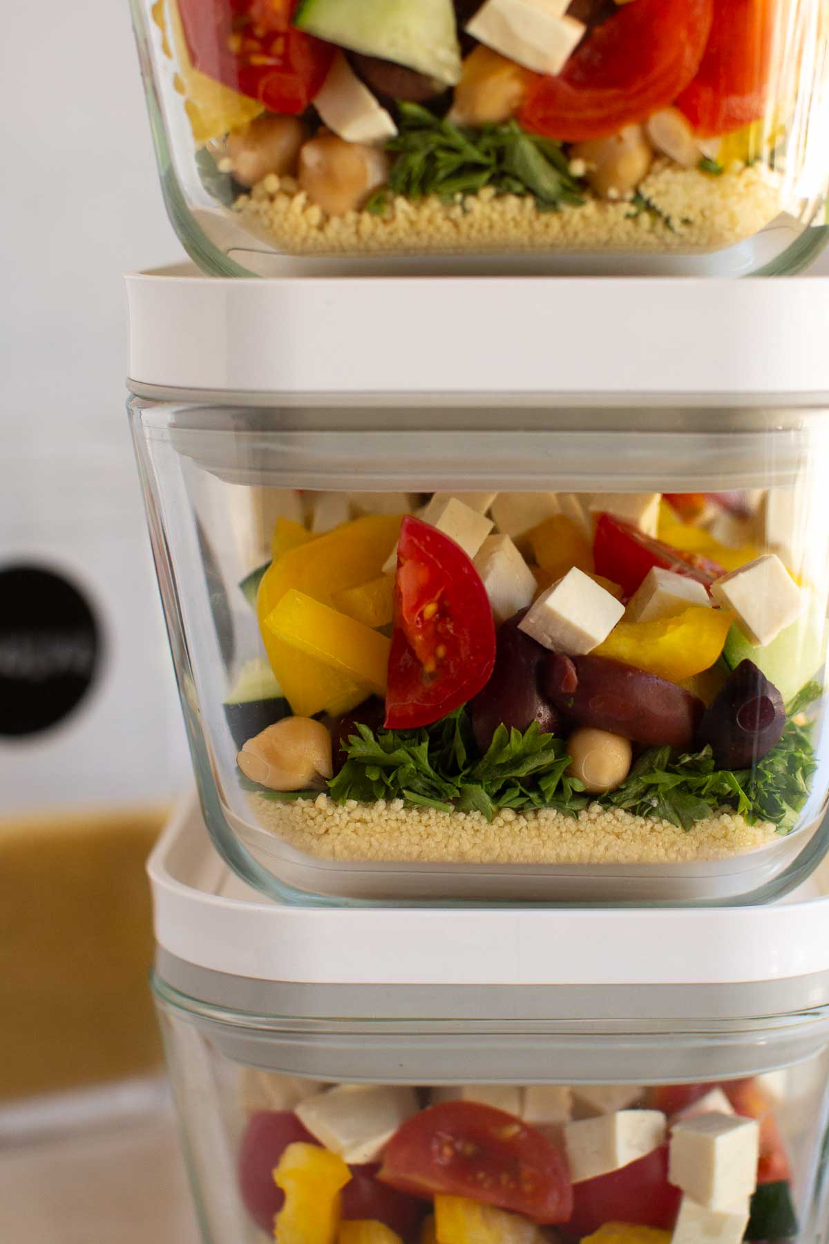 Stacked containers filled with couscous, veggies, kalamata olives, and tofu.