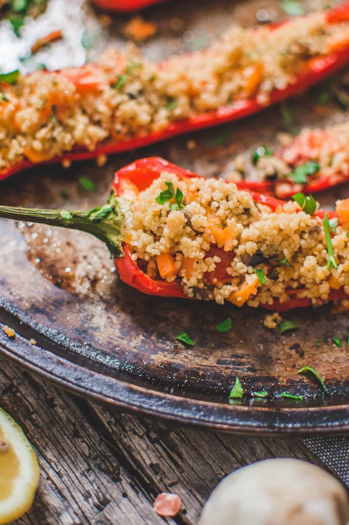 Couscous stuffed pepper with carrots, mushrooms, and parsley on a rustic baking tray.