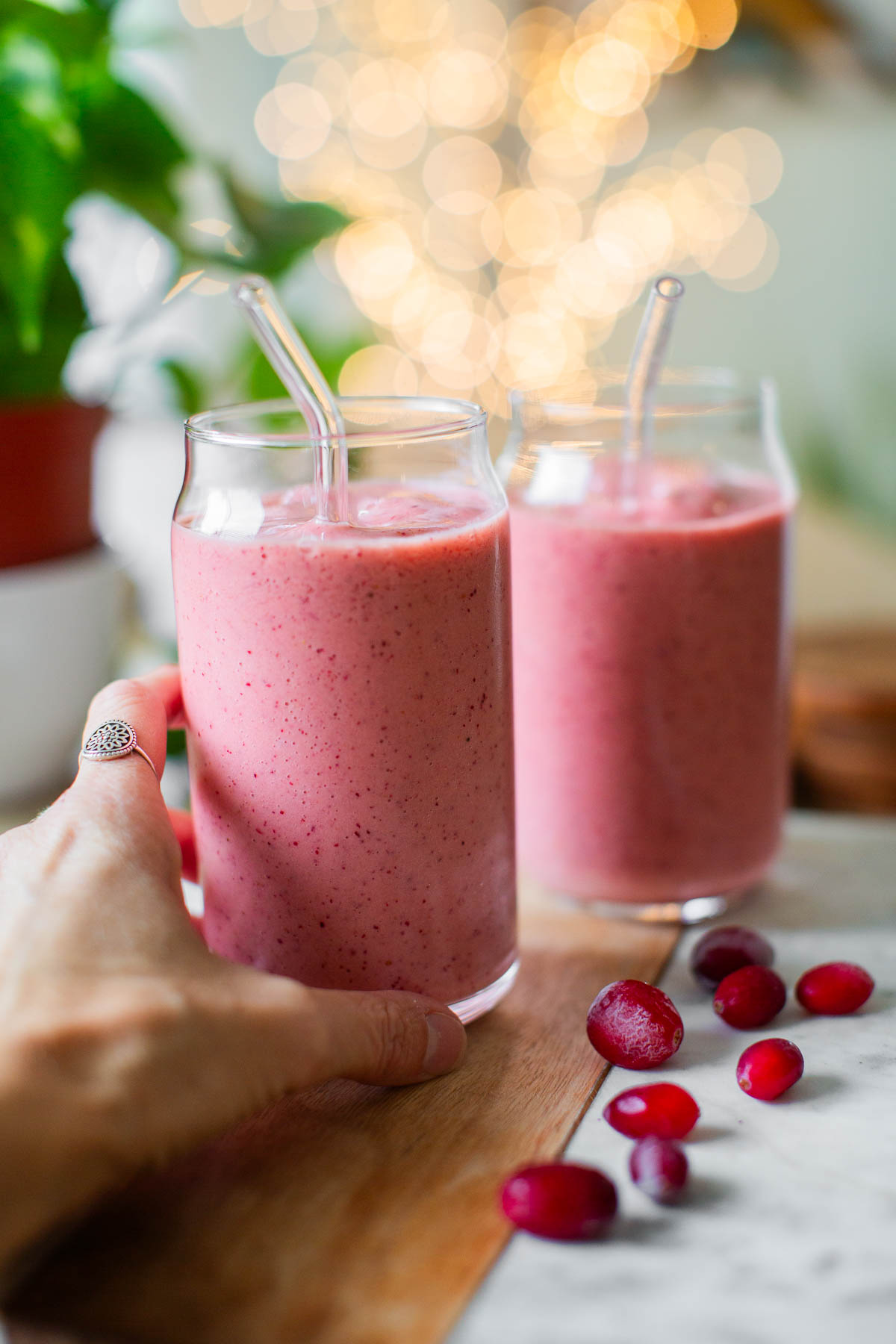 A hand reaching for a glass of pink cranberry smoothie, a healthy vegan snack option.