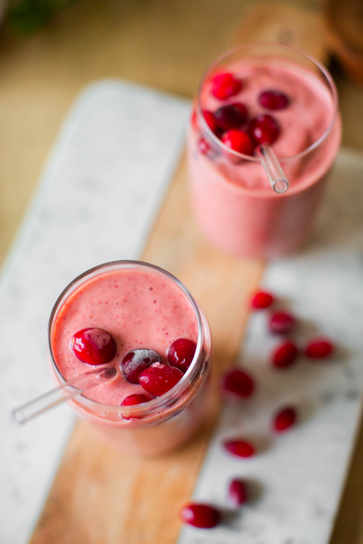 Two glasses of frozen cranberries smoothies topped with extra frozen cranberries.