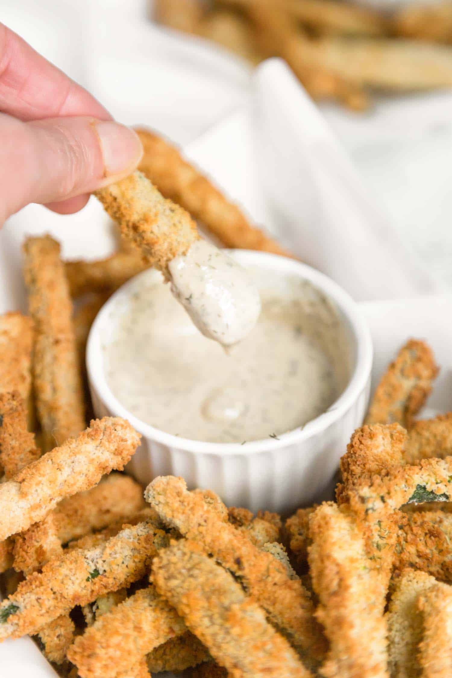 A zucchini fry being dipped into a creamy sauce, perfect for healthy vegan snacking.