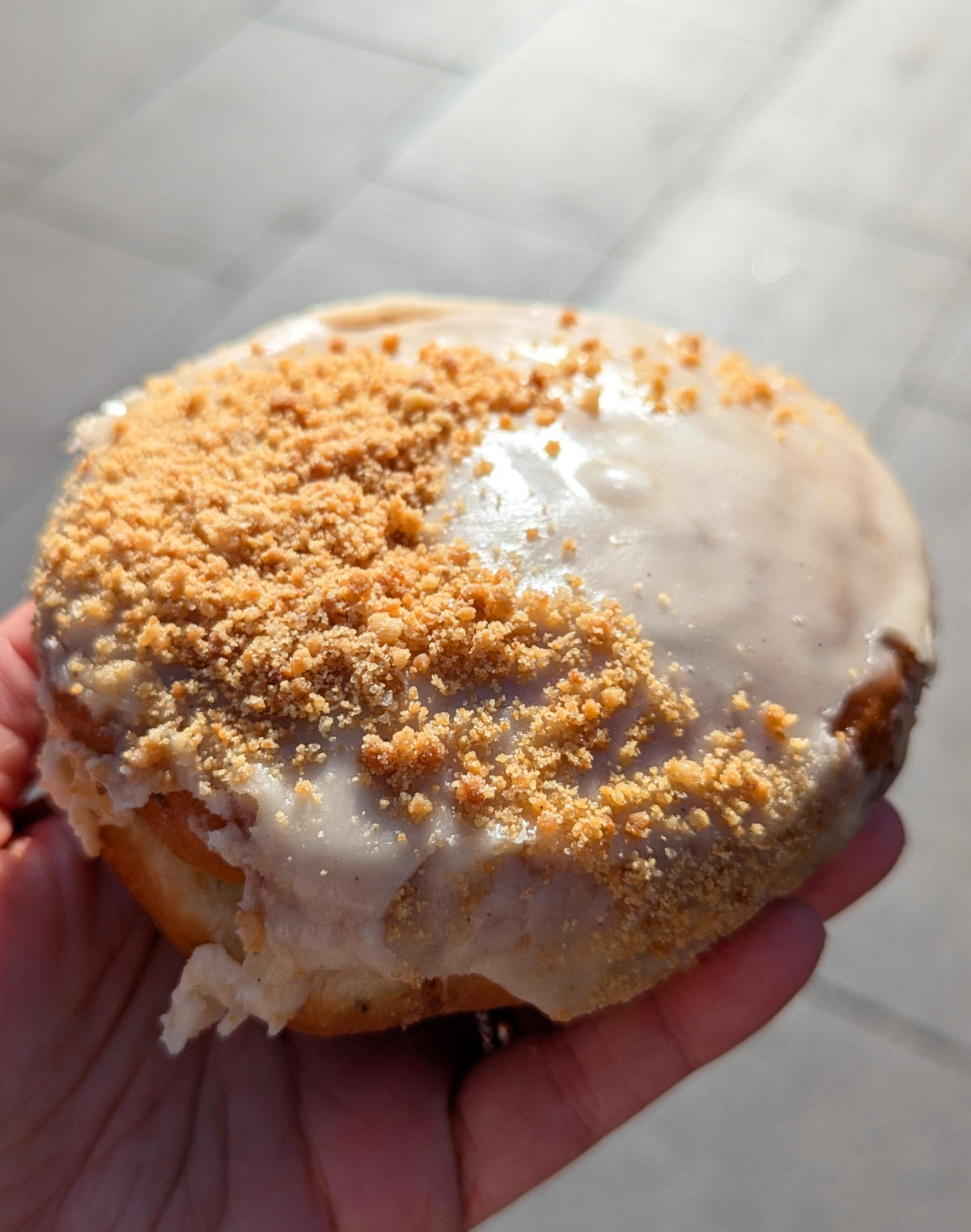 A hand holding a vegan cinnamon roll donut from Crosstown in London.