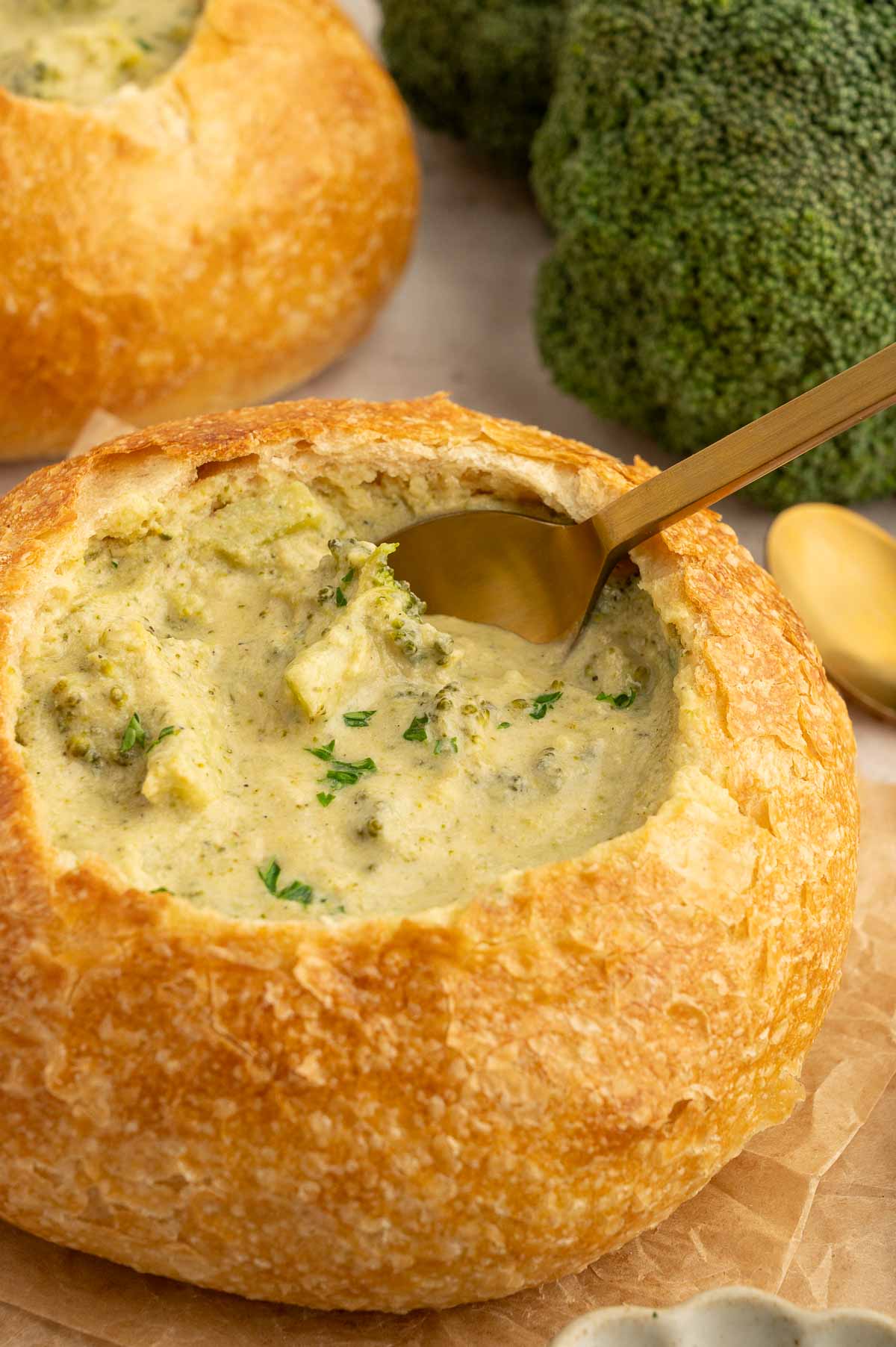 Bread bowl filled with dairy-free cream of broccoli soup and a dipping spoon.