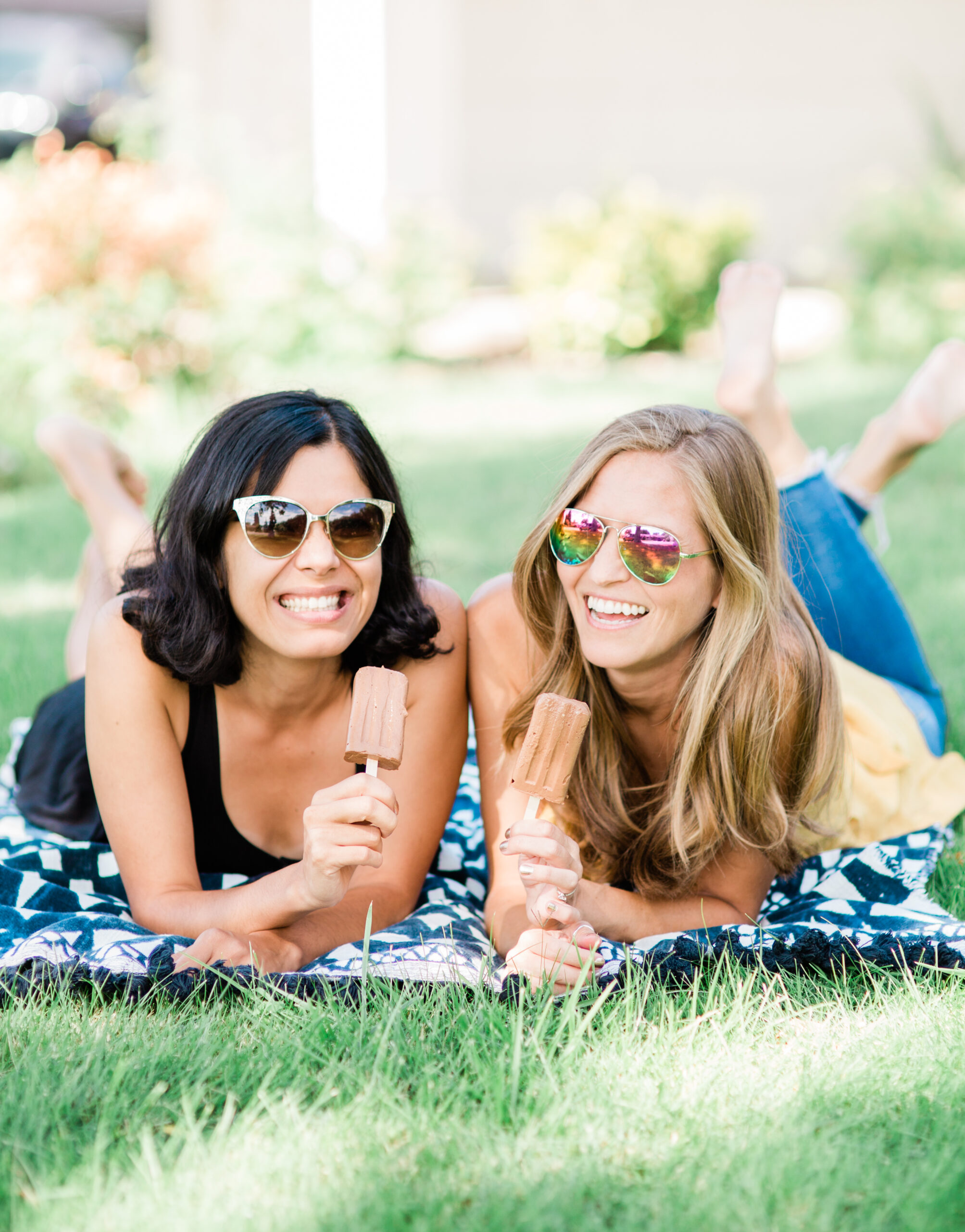 Toni Okamoto and Michelle Cehn laying on a picnic blanket, smiling and holding fudgesicles.