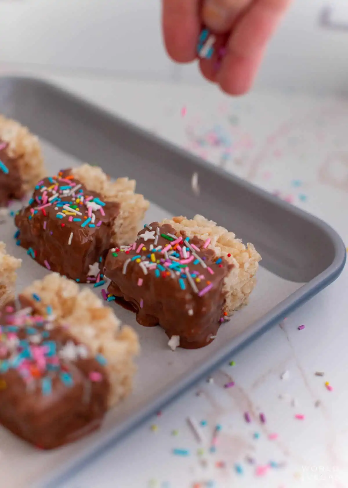 A hand adding sprinkles to melted chocolate covered rice krispies.