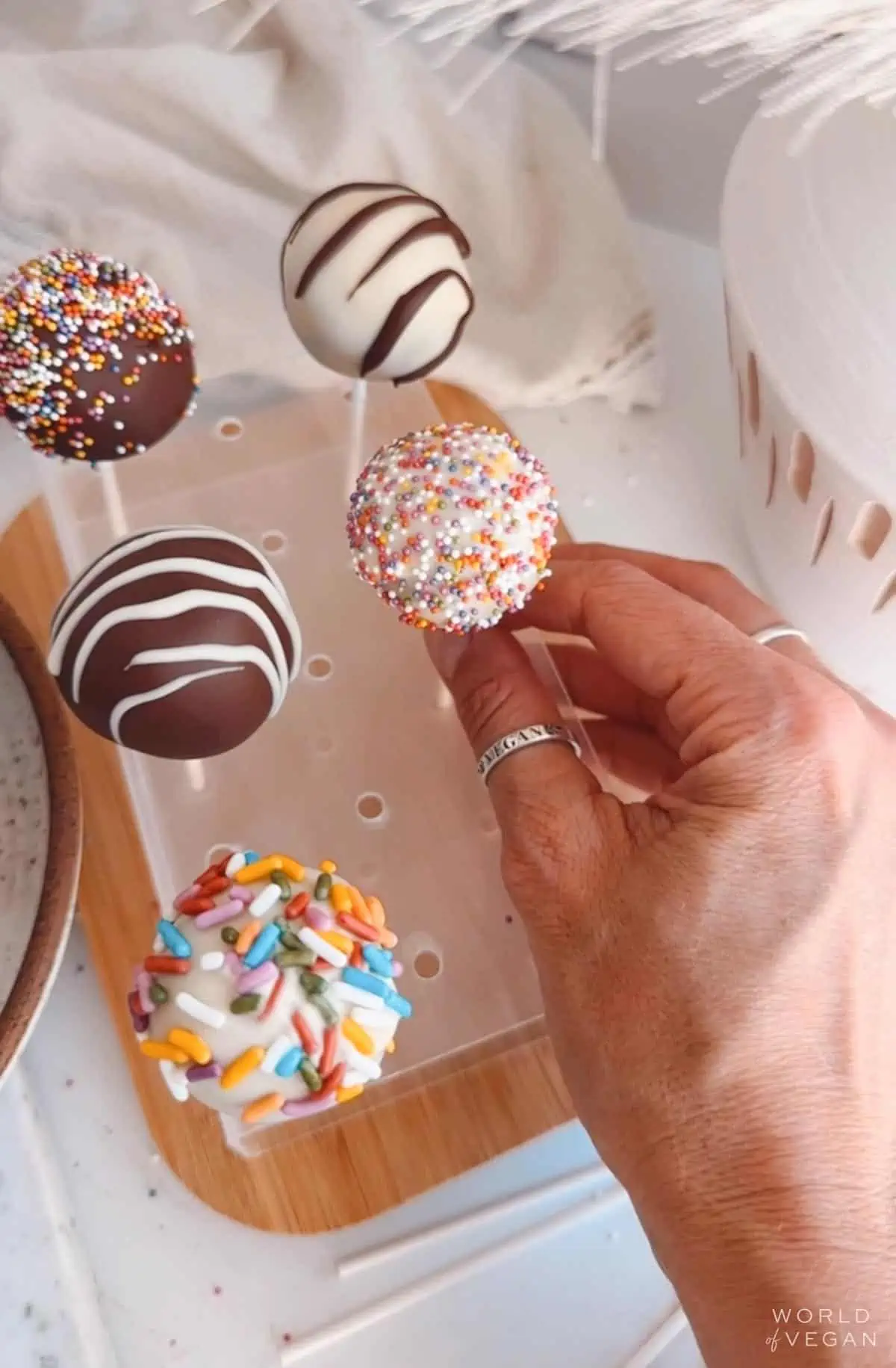 A cake pop stand with 5 colorfully decorated vegan cake pops with chocolate drizzle and sprinkles.