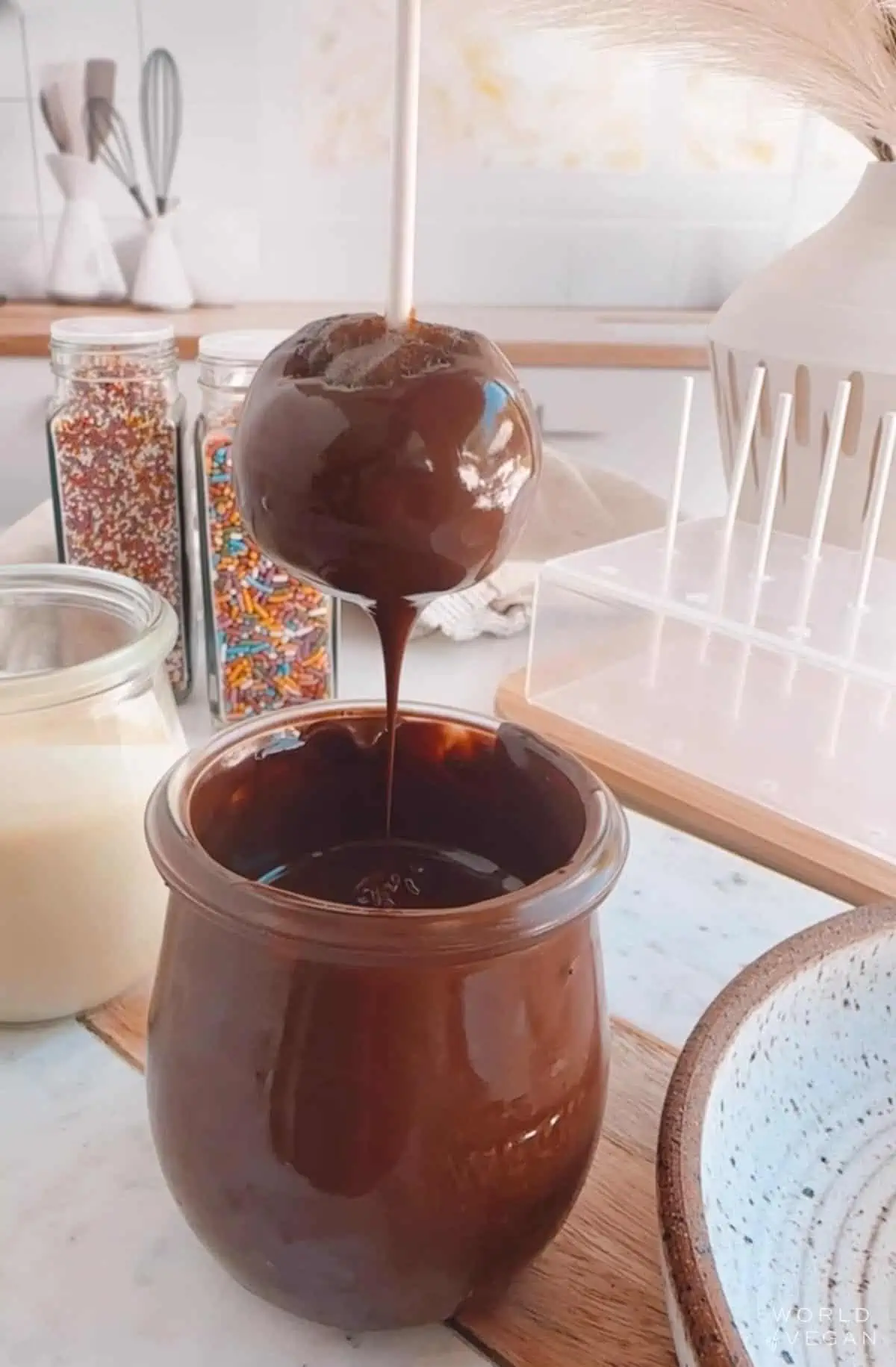 Showing how to dip a cake pop in melted chocolate to coat.