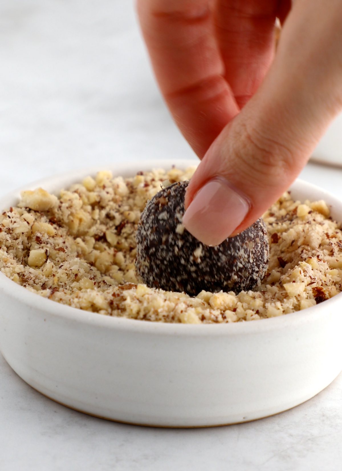 A vegan protein ball being rolled in a bowl of chopped nuts.