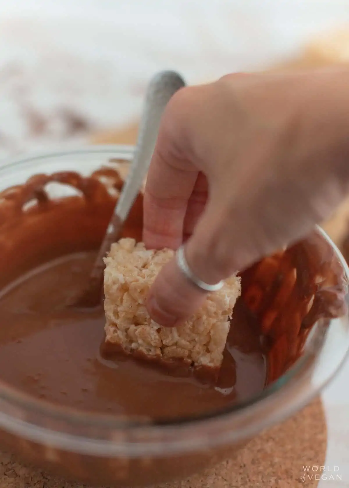 A hand dipping a vegan rice crispy treat into melted chocolate.