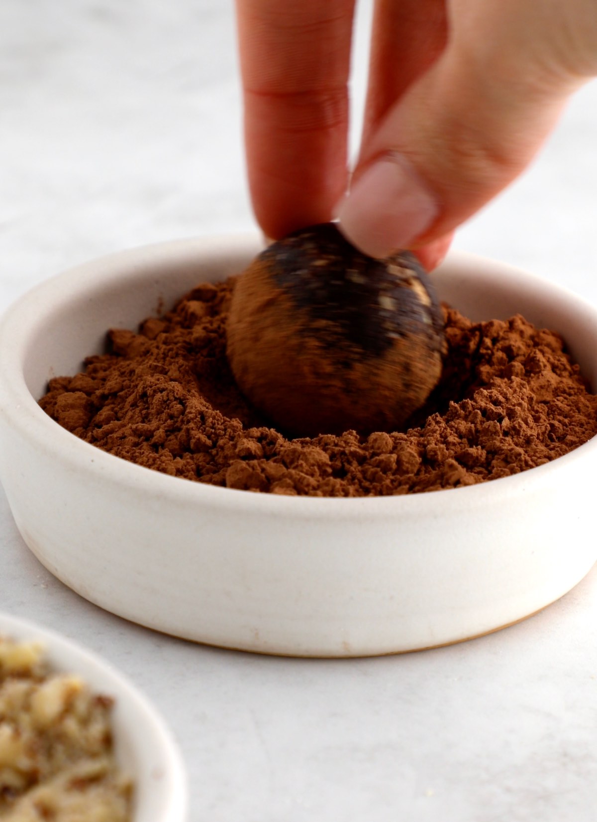 A vegan protein ball being rolled in cocoa powder in a bowl.
