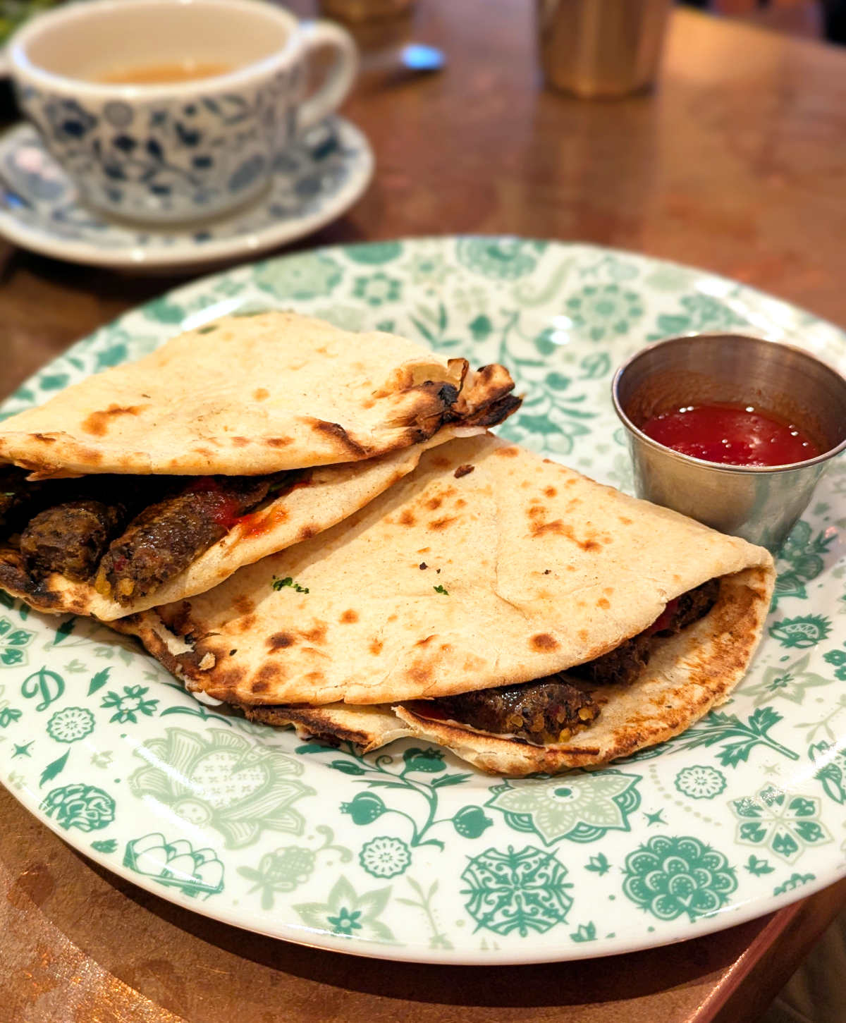 Two vegan naan rolls filled with vegan sausage and a side of chutney.