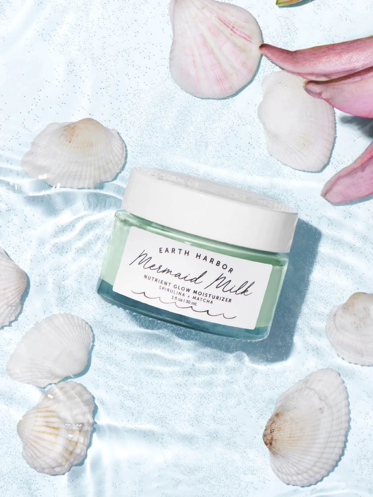 A jar of Earth Harbor mermaid milk moisturizer in a pool of water with flower petals around it.