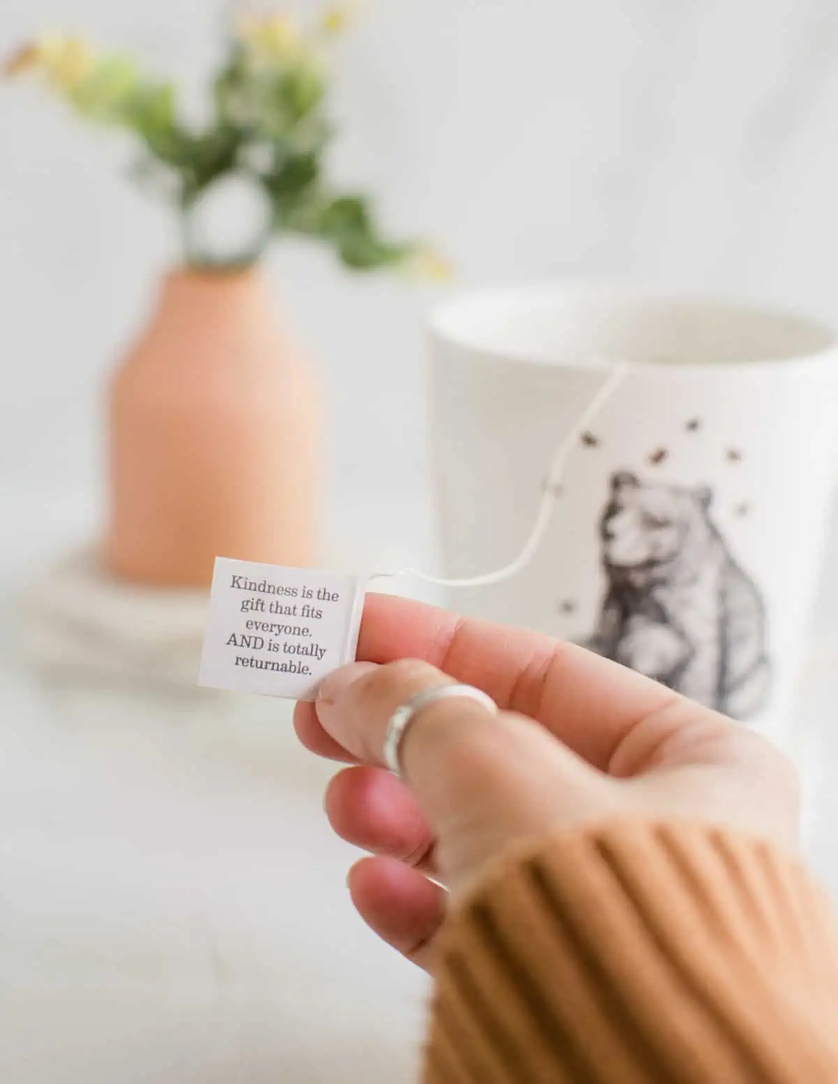 Holding up an Earth Mama vegan tea tag that has an inspiring message about kindness.