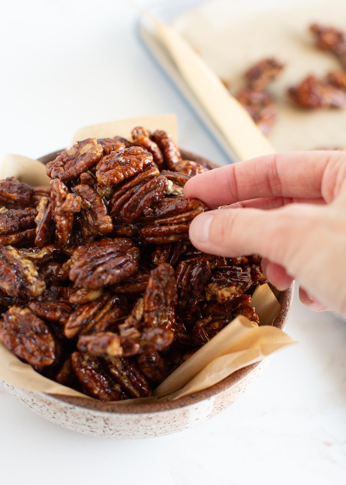 A hand reaching for a vegan candied pecan from a bowl.